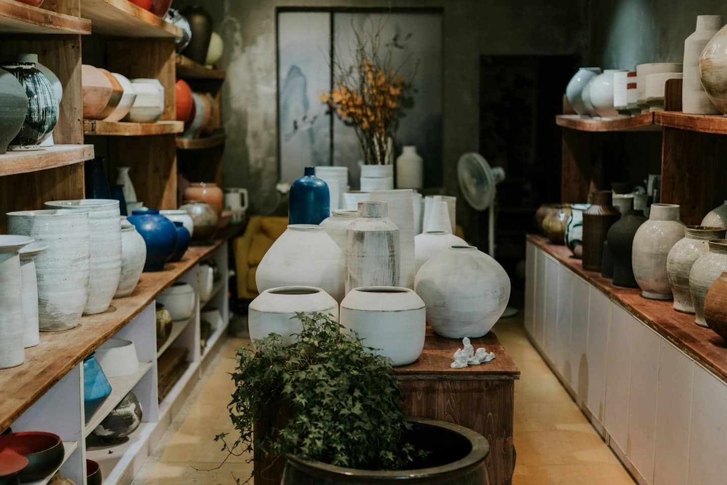 Ceramiche artigianali esposte su mensole e tavolo di legno.