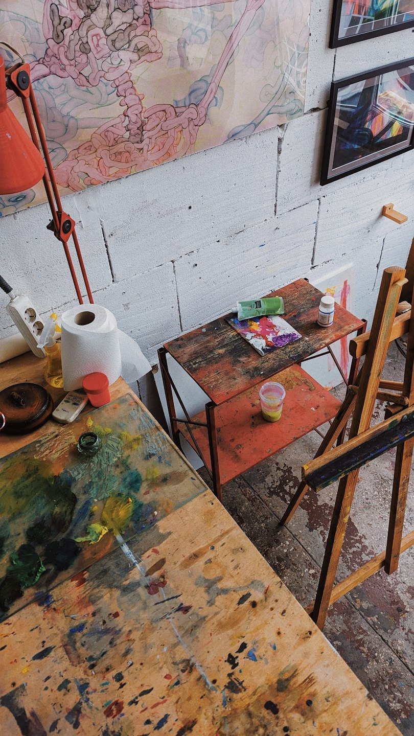 Banco da lavoro di un artista con materiali per pittura e opere astratte alle pareti.