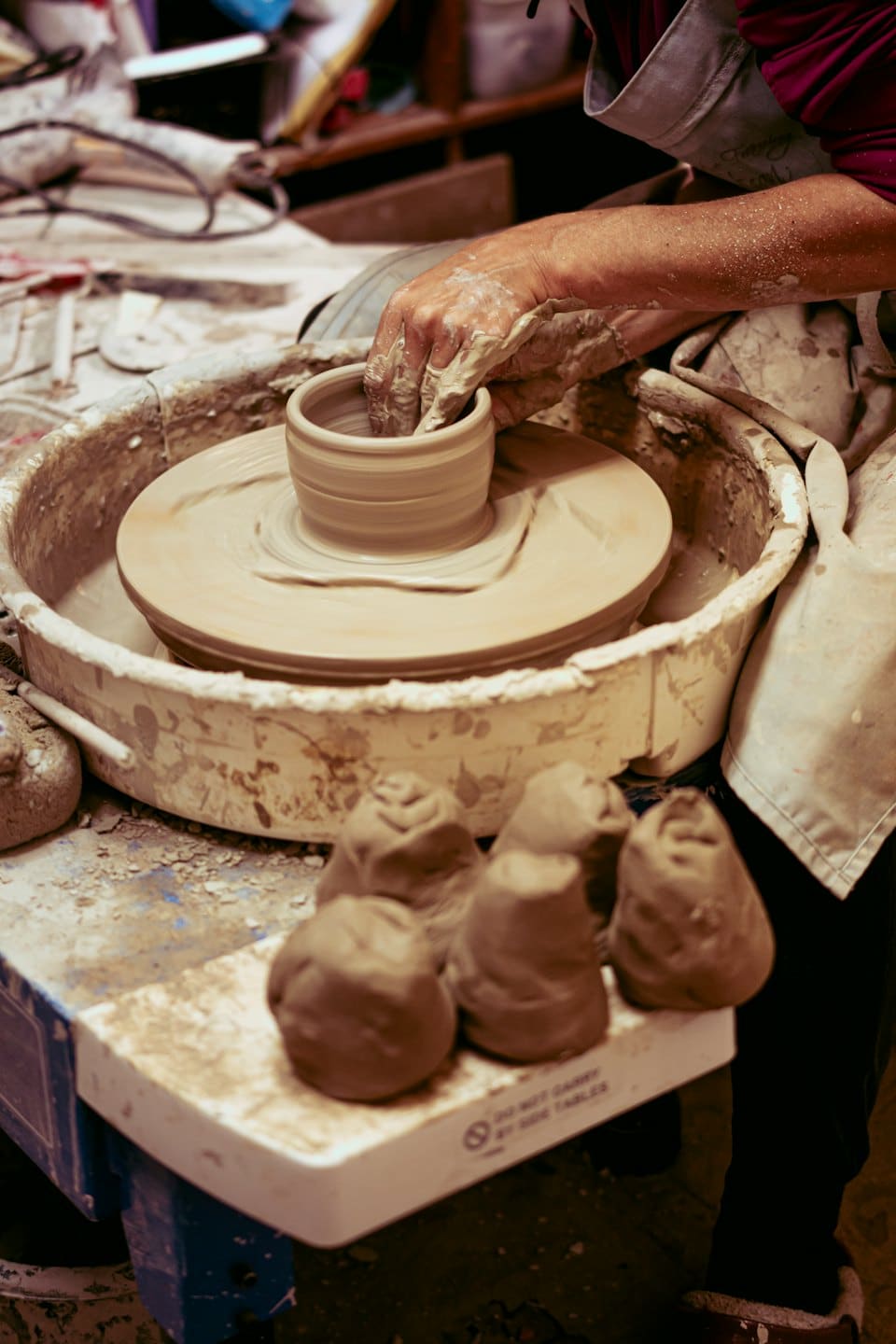 Mani sporche di argilla che modellano un vaso su un tornio da vasaio.