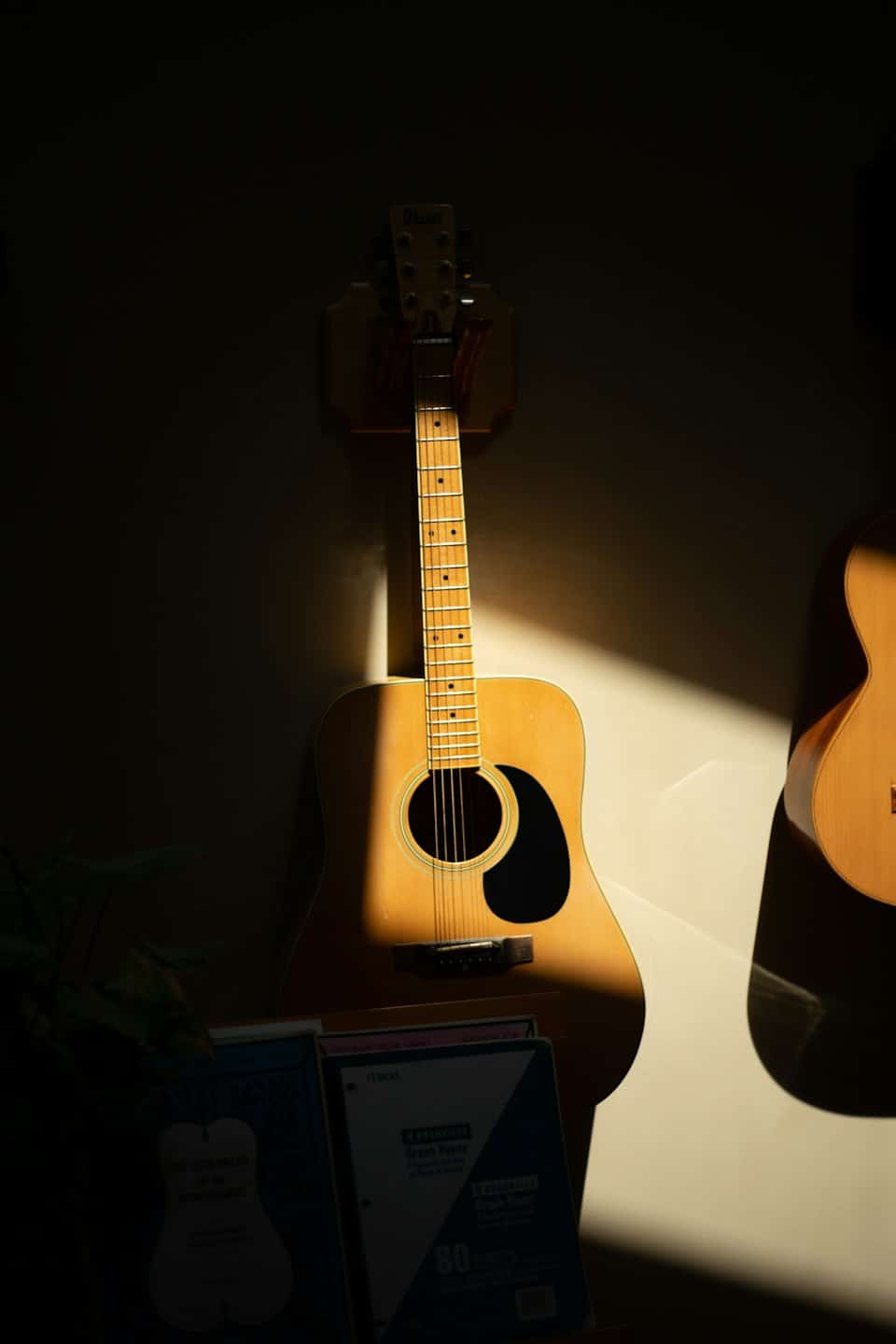 Chitarre acustiche appese a una parete sopra libri di musica impilati.